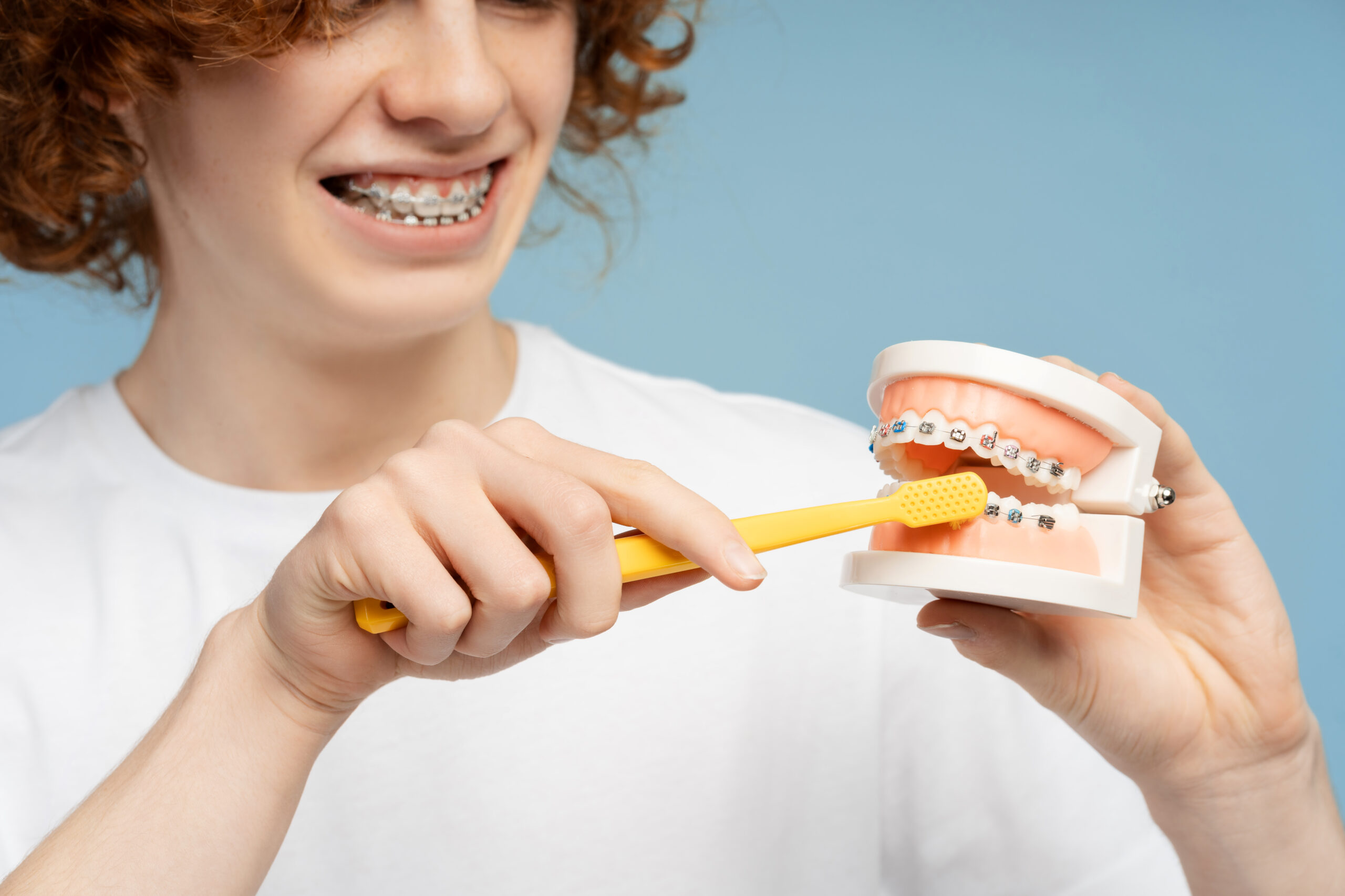 Teen brushing a set of teeth with braces.